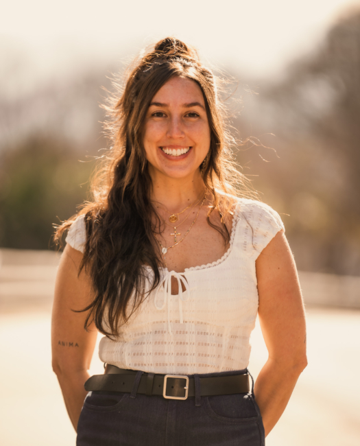 Smiling Wye Hill Kitchen & Brewing team member in a white top outdoors at golden hour in downtown Raleigh