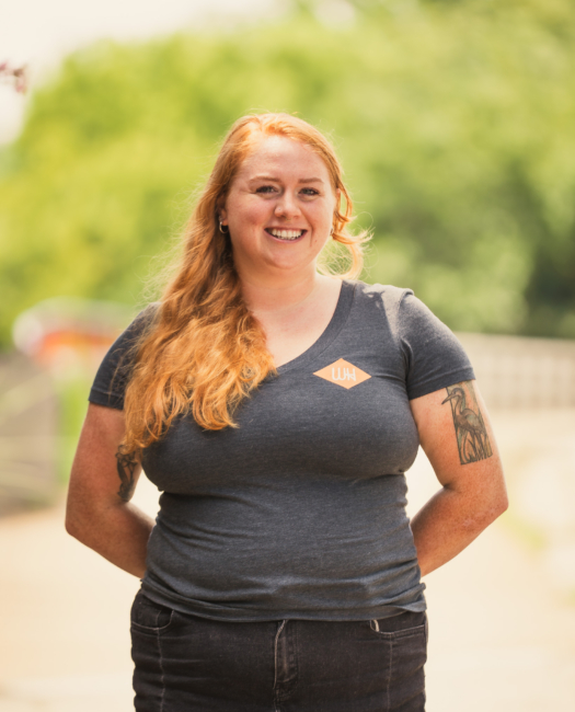 Smiling Wye Hill Kitchen & Brewing team member in a gray Wye Hill t-shirt outdoors in downtown Raleigh