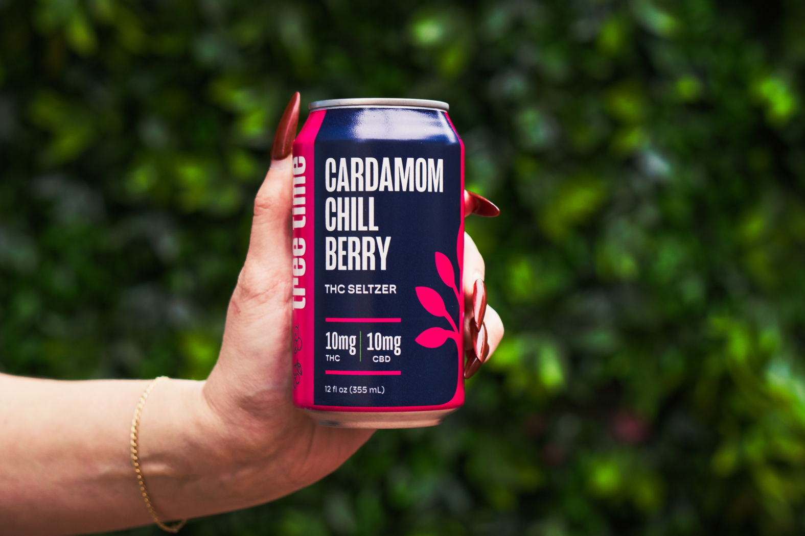 Hand holding a Cardamom Chill Berry Tree Time THC seltzer can against a leafy green background